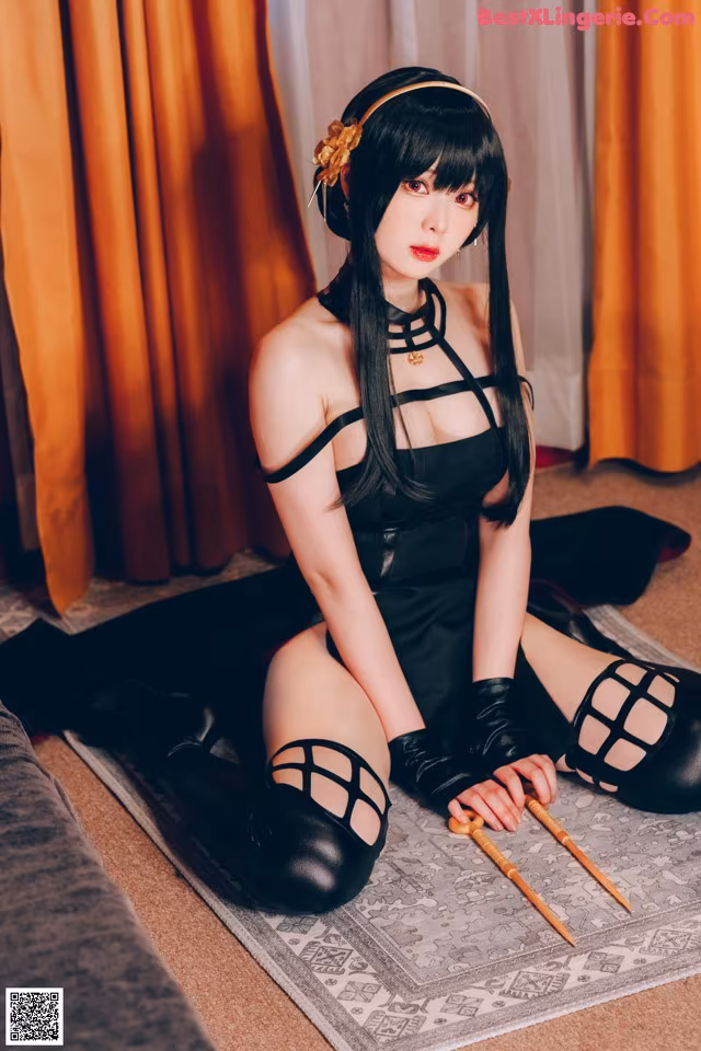 A woman in a black dress sitting on the floor with chopsticks.