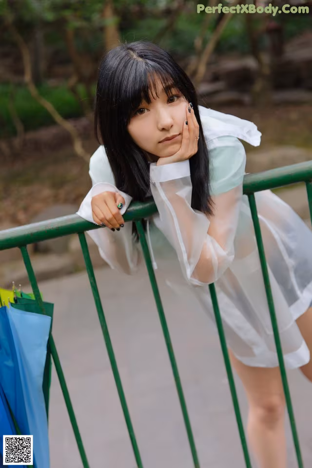 A woman in a white dress leaning against a green fence.