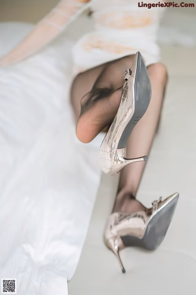 A woman in a wedding dress and high heels sitting on a bed.
