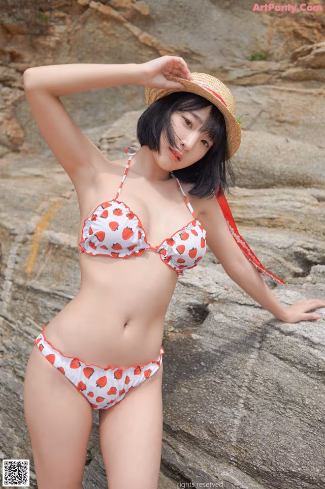 A woman in a bikini and a straw hat posing on a rock.