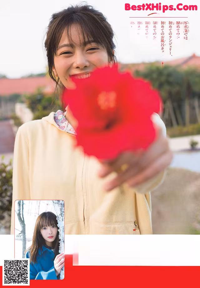 A woman holding a red flower in front of her face.