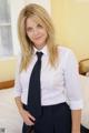 A woman in a white shirt and black tie posing on a bed.