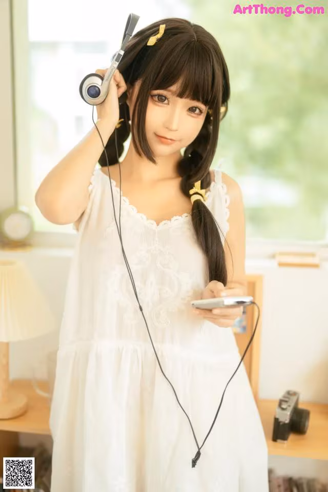 A woman in a white dress holding a cell phone and headphones.