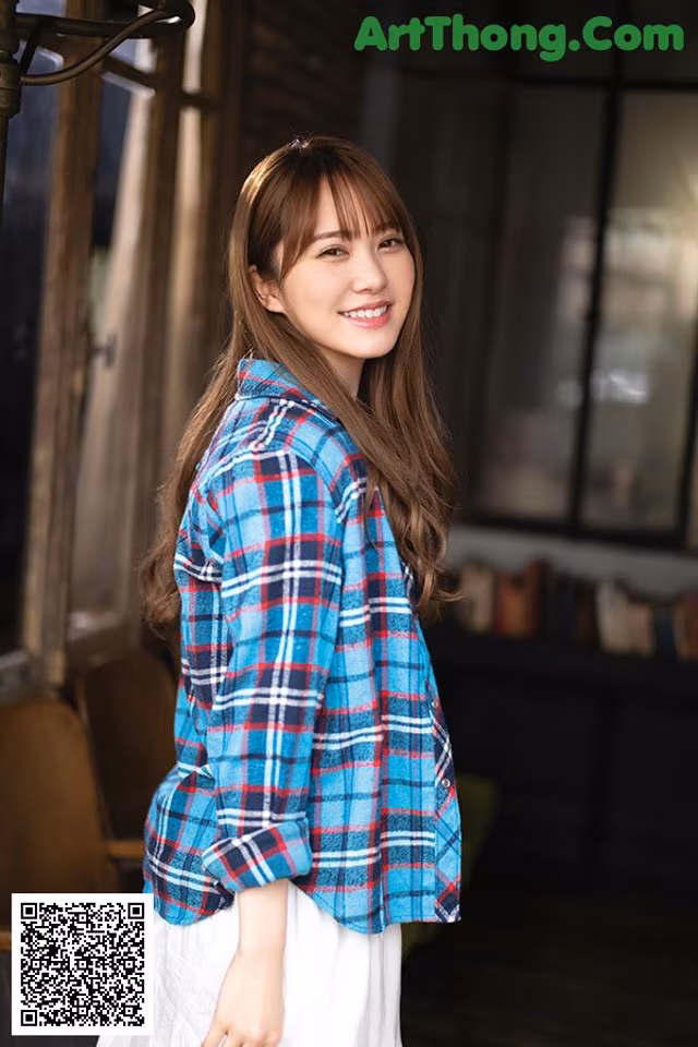 A woman wearing a blue and red plaid shirt and white skirt.