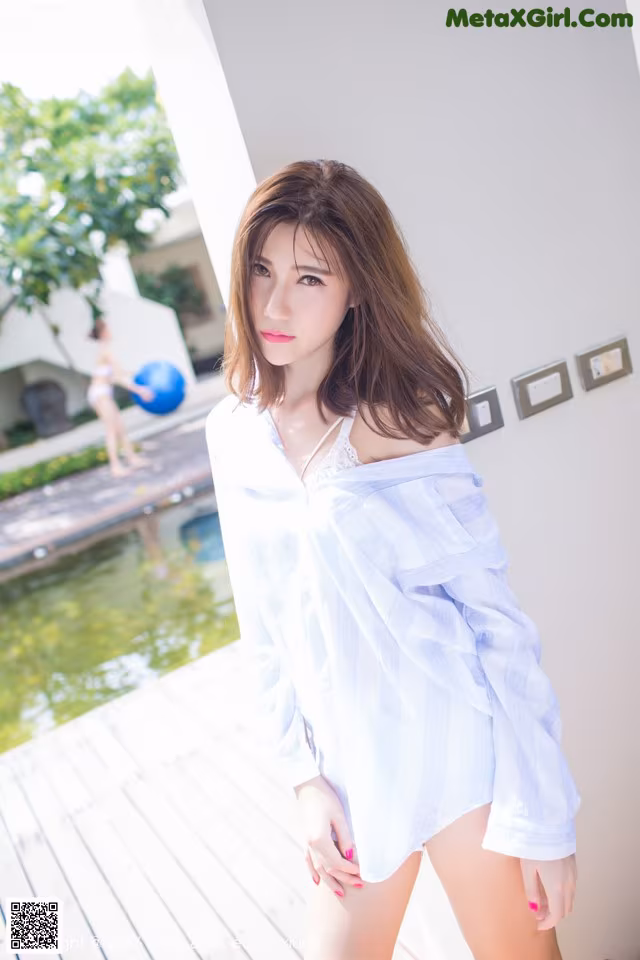 A woman in a white shirt is posing by a pool.