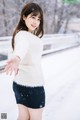 A woman in a white sweater and black skirt standing in the snow.