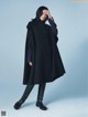 A woman in a black coat and black boots posing for a magazine.