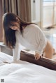 A woman in a white shirt is bending over a bed.