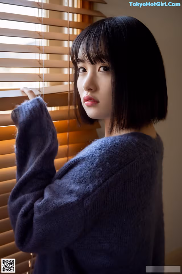A woman standing in front of a window with blinds.