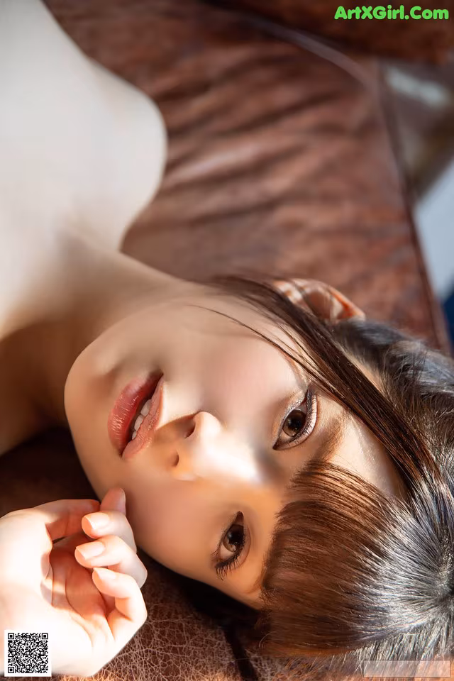 A woman laying on top of a brown couch.