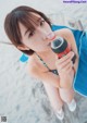 A woman sitting on a beach holding a bottle of soda.