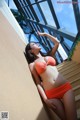 A woman in an orange bikini leaning against a wall.