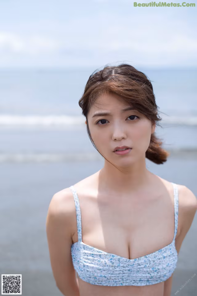 A woman in a blue and white bikini standing on a beach.