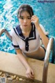 A woman in a sailor outfit sitting on the edge of a swimming pool.